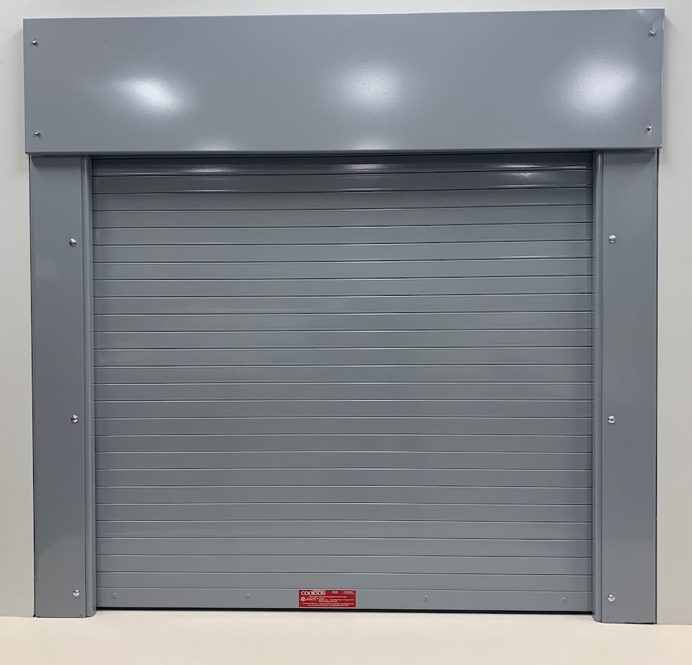 Grey fire-rated rolling shutter with hood and guides over a counter opening